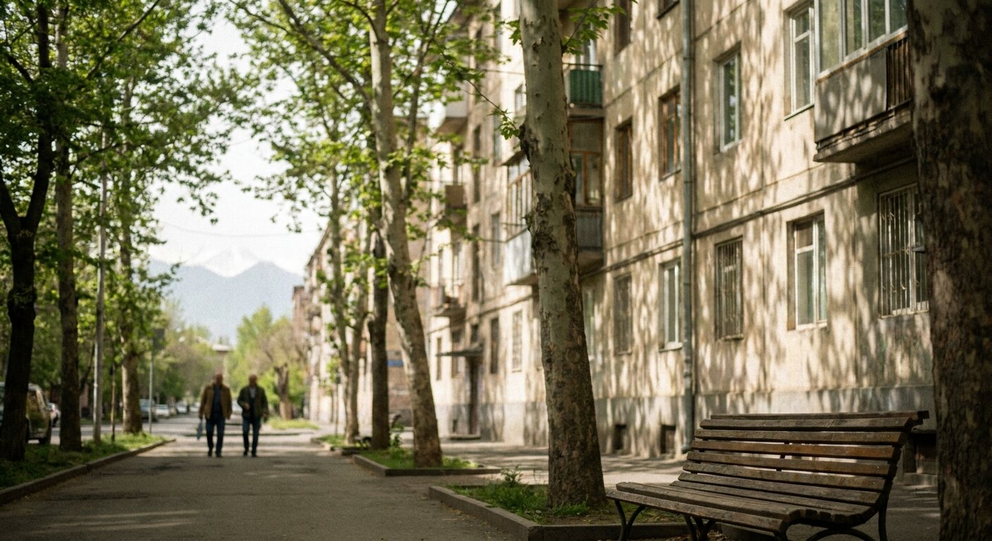A tree-lined city street in late May morning light — plane trees casting dappled shadow on a pale Soviet-era building facade, a park bench visible at the edge of the frame, the pale suggestion of distant mountains at the horizon. Two figures seen from behind at a distance, slightly out of focus, walking together along the pavement. The atmosphere is an ordinary city day experienced without agenda. No text, no signs, no writing visible anywhere. Photorealistic, cinematic, soft May morning light, documentary photography style, shallow depth of field, muted warm-green palette.